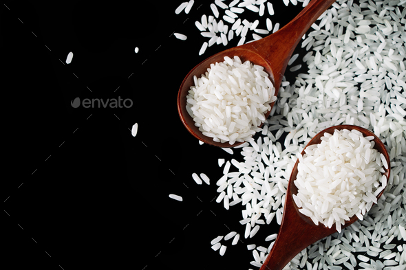 White uncooked rice in wooden spoons on black background. Raw grains of long rice. - Stock Photo - Images