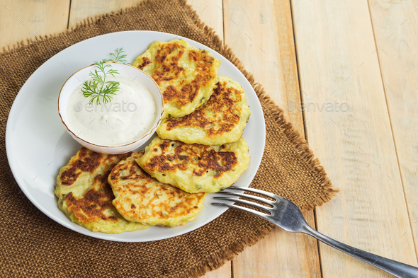 Vegan zucchini pancakes in plate and cream sauce on wooden background. Healthy vegan diet food. - Stock Photo - Images