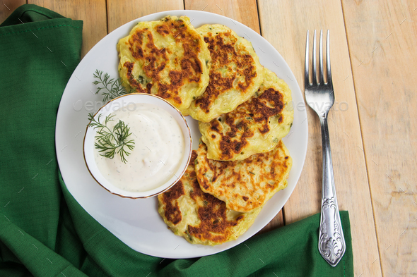Vegan green zucchini pancakes in plate and creamy sauce. Healthy vegan diet food. - Stock Photo - Images