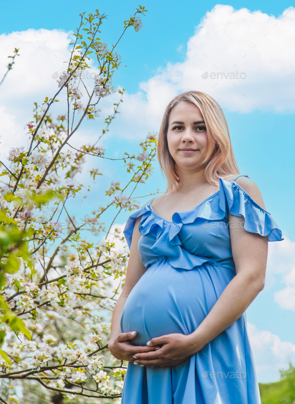 Pregnant woman in the garden of flowering apple trees. Selective focus. - Stock Photo - Images