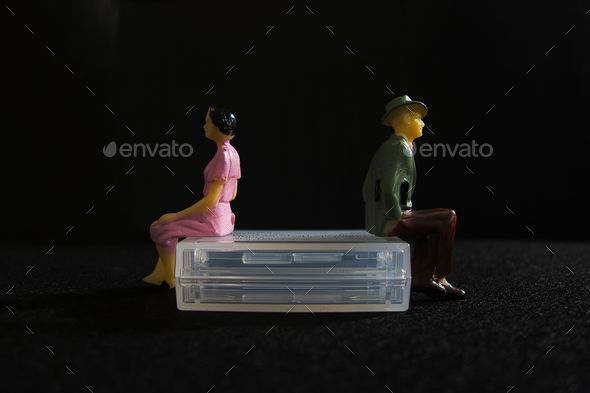 Plastic figures of a man and a woman sitting separately back to back on a chair, a broken marriage