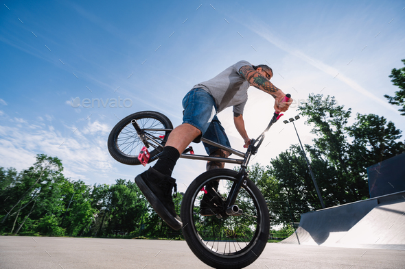 Low-angle view of a tattooed mature man performing freestyle bmx tricks on a bike in a skate park.