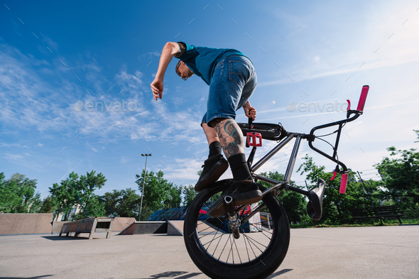 A mature tattooed professional bike rider is balancing on on wheel with his bmx in a skate park. - Stock Photo - Images