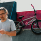 A bmx bike in a skatepark with a mature urban tattooed man using his phone in a blurry foreground. - PhotoDune Item for Sale