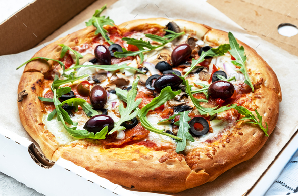 Hot Pizza in box with salami sausage, mozzarella cheese, mushrooms, olives, tomato sauce and arugula - Stock Photo - Images