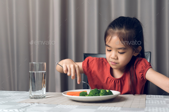 Asian little girl eating healthy vegetables with relish. - Stock Photo - Images
