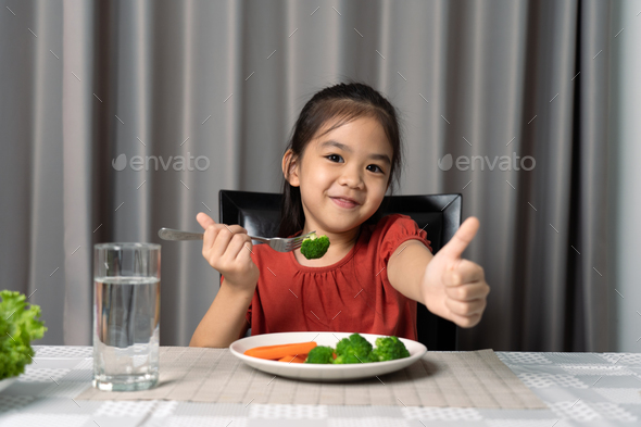 Cute little girl showing thumb showing eating healthy vegetables. - Stock Photo - Images