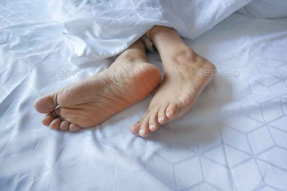  young Woman lying with bare feet in bed, - Stock Photo - Images