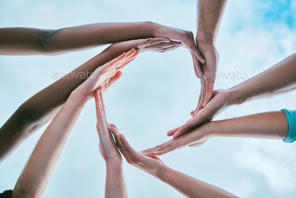 Closeup of diverse group of people from below joining hands together to form circle shape expressin