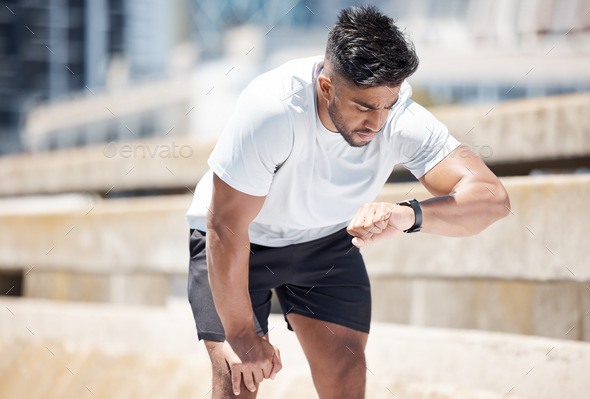 Athletic young mixed race man looking at his watch while exercising  outdoors. Handsome mixed race m