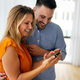 Smiling couple embracing while using a smartphone. People sharing social media on mobile phone. - PhotoDune Item for Sale