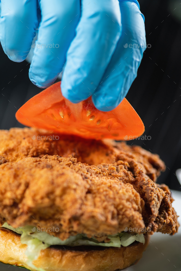 Chef Hand placing Tomato slice onto a Crispy Fried Chicken. - Stock Photo - Images