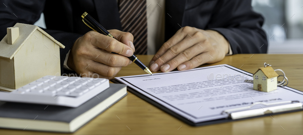 Real estate agent holding home and signing a contract about the agreement of real property on desk,