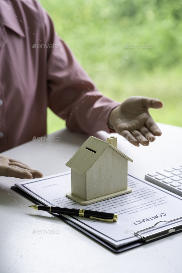Real estate agent holding home and signing a contract about the agreement of real property on desk,