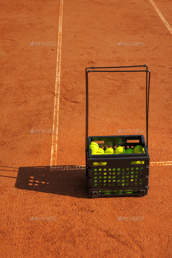 tennis green balls in black basket court made of red clay soil with markings for game or competition - Stock Photo - Images