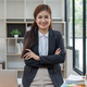 Young successful woman entrepreneur or an office worker stands with crossed arms near a desk in a - PhotoDune Item for Sale