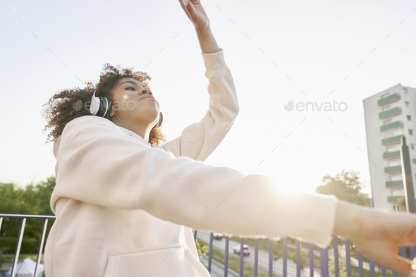 Black woman wearing headphones and dancing on the bridge - Stock Photo - Images