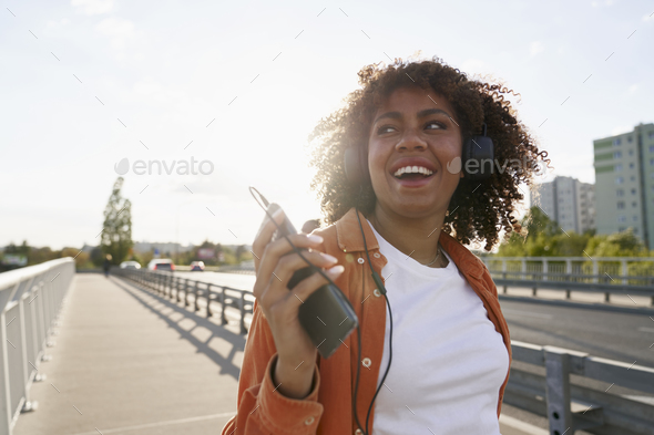 Black woman wearing headphones and walking on the bridge - Stock Photo - Images