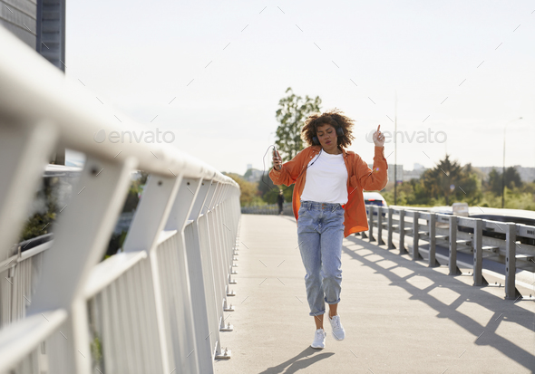 Wide shot of black woman wearing headphones and dancing on the bridge - Stock Photo - Images