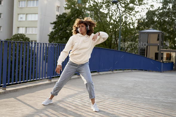 Wide shot of black woman wearing headphones and dancing on the bridge - Stock Photo - Images
