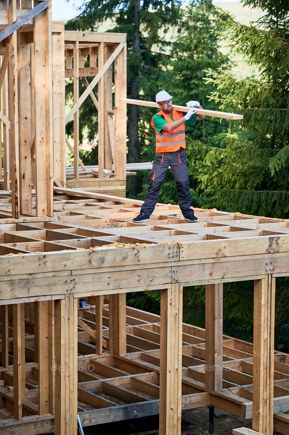 Carpenter holding large beam while builds wooden frame house near the