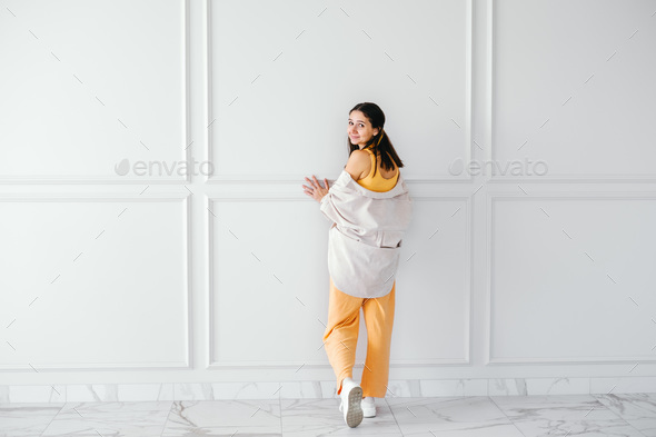 Beautiful young brunette shows off  summer outfit  shirt and  suit with sneakers on beige wall - Stock Photo - Images