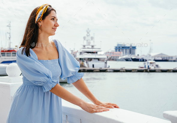 Portrait of young beautiful woman in blue dress on the shore against the background of yachts.  - Stock Photo - Images