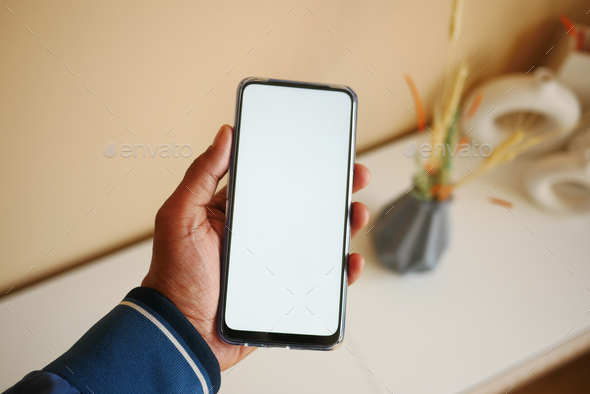  hands holding cell telephone with empty screen against home background  - Stock Photo - Images