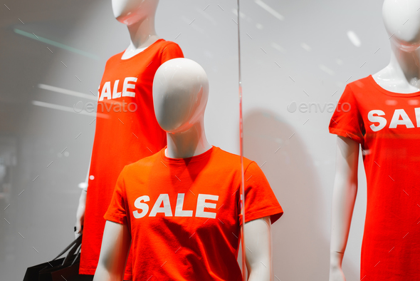 Mannequins in red bright t-shirts with the inscription SALE standing in a shop window.