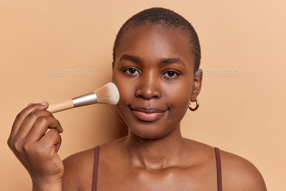 Beauty portrait of young woman applies blusher with cosmetic brush puts on decorative makeup looks