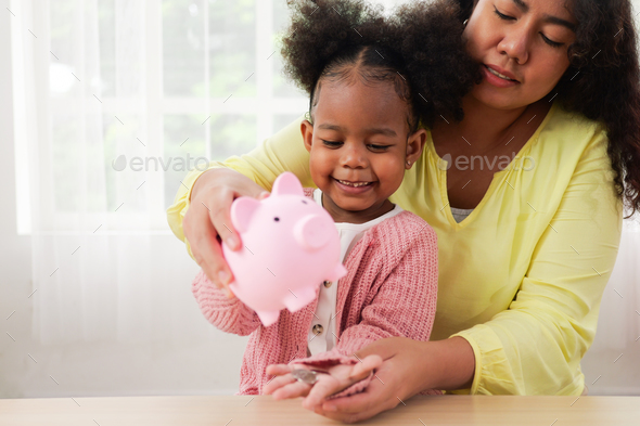 Daughter and happy mother saving money putting coin into piggy bank
