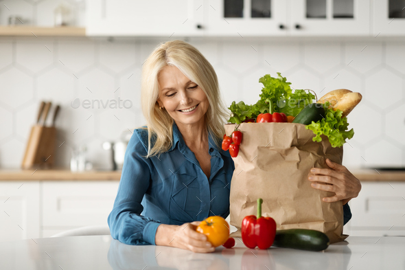 Organic Food Delivery. Happy Mature Lady Unpacking Bag With Groceries In Kitchen - Stock Photo - Images
