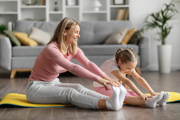 Joyful young mother and little daughter stretching legs together at home - Stock Photo - Images