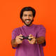 Happy indian guy playing video game, holding joystick, orange background - PhotoDune Item for Sale