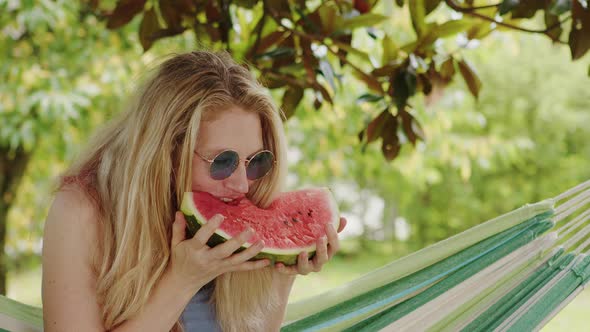 smiling blonde woman wearing sunglasses, eating a slice of watermelon