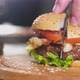 chef knife cuts Burger on a wooden round tray on the background of the kitchen. - VideoHive Item for Sale
