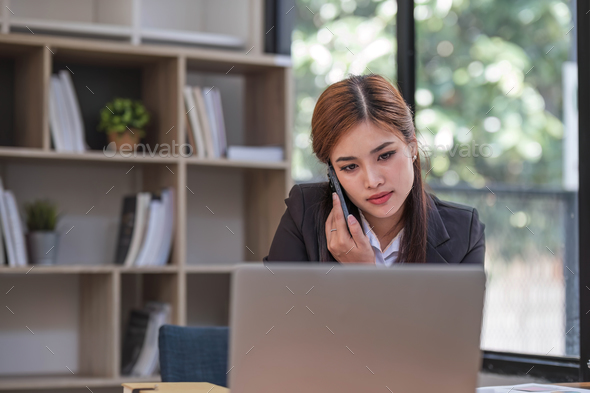 Asian businesswoman in formal suit in office happy and cheerful during using smartphone and working - Stock Photo - Images