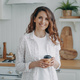 Smiling hispanic woman with paper cup of coffee standing in cozy modern kitchen, looking at camera - PhotoDune Item for Sale