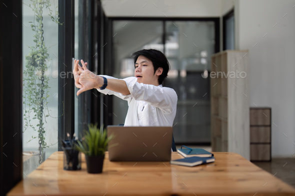 Stretching oneself asian business man with laptop in cafe. tried from work,  stretch oneself Stock Photo by nateemee