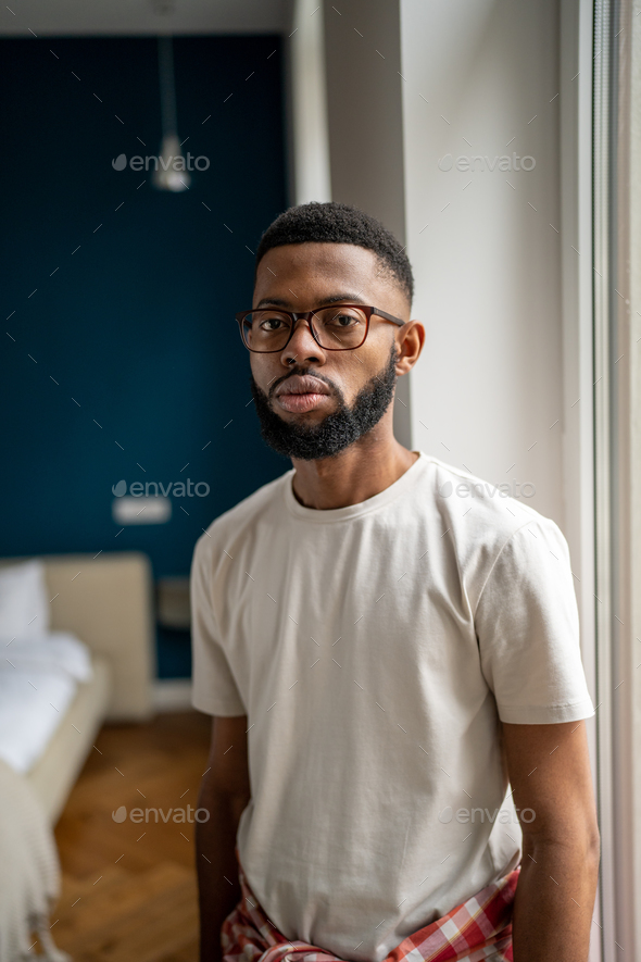 Portrait serious african american bearded man in eyeglasses in white t-shirt near window at home - Stock Photo - Images
