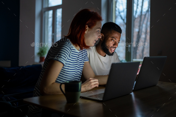 Happy diverse couple have small online business at home work on laptops in evening - Stock Photo - Images