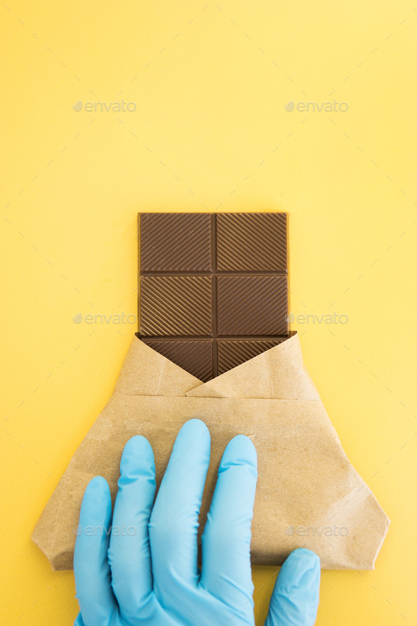 Bar of milk chocolate in a wrapper is held by a hand in a medical glove. World chocolate day
