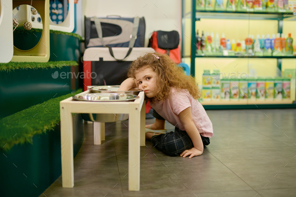 Sad little girl sitting nearby big feed bowl dreaming about dog at pet shop - Stock Photo - Images