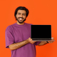 Positive indian man showing laptop with blank screen on orange - PhotoDune Item for Sale