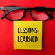 Top view glasses and sticky note with the word LESSONS LEARNED on red background. - PhotoDune Item for Sale