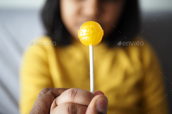 child holding yellow color lollipop candy  - Stock Photo - Images