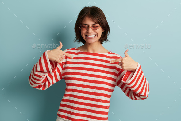 Confident carefree young woman smiling and pointing at herself in studio - Stock Photo - Images