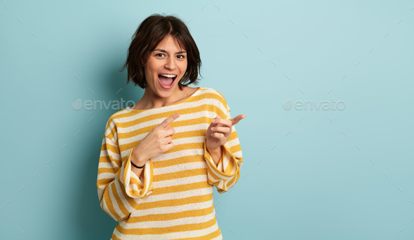 Delighted young ethnic woman pointing away and smiling in studio - Stock Photo - Images