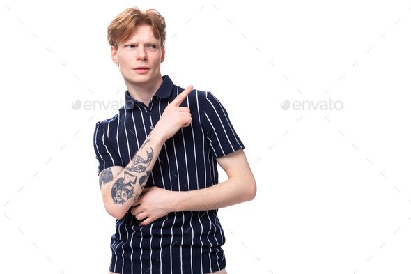young European blond guy in a striped polo shirt with a tattoo shows his hand to the side on a white