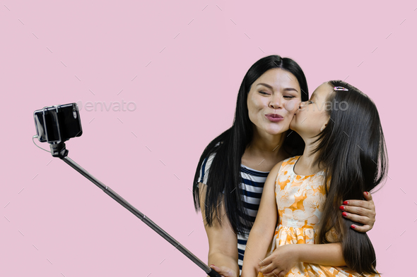 Mother and her daughter are making a selfie on smartphone using the stick. - Stock Photo - Images